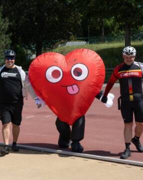 Maskotka serce na torze Osoby trzymające maskotkę w serce na torze sportowym